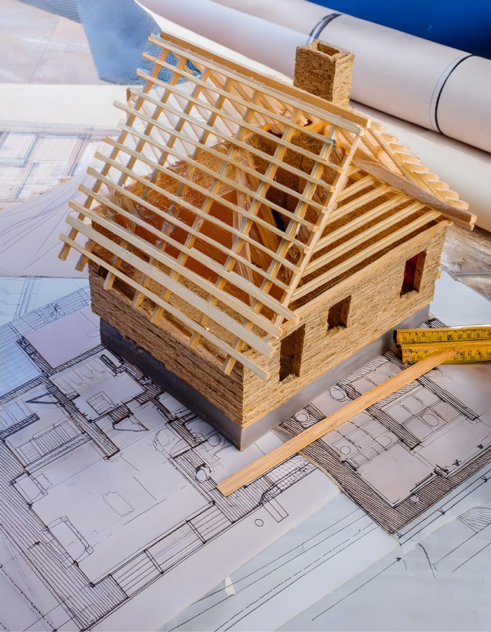 Maquette de maison avec charpente en bois posée sur des plans de construction.