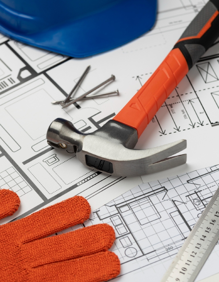 Marteau, clous, casque et gants de chantier disposés sur des plans de construction.